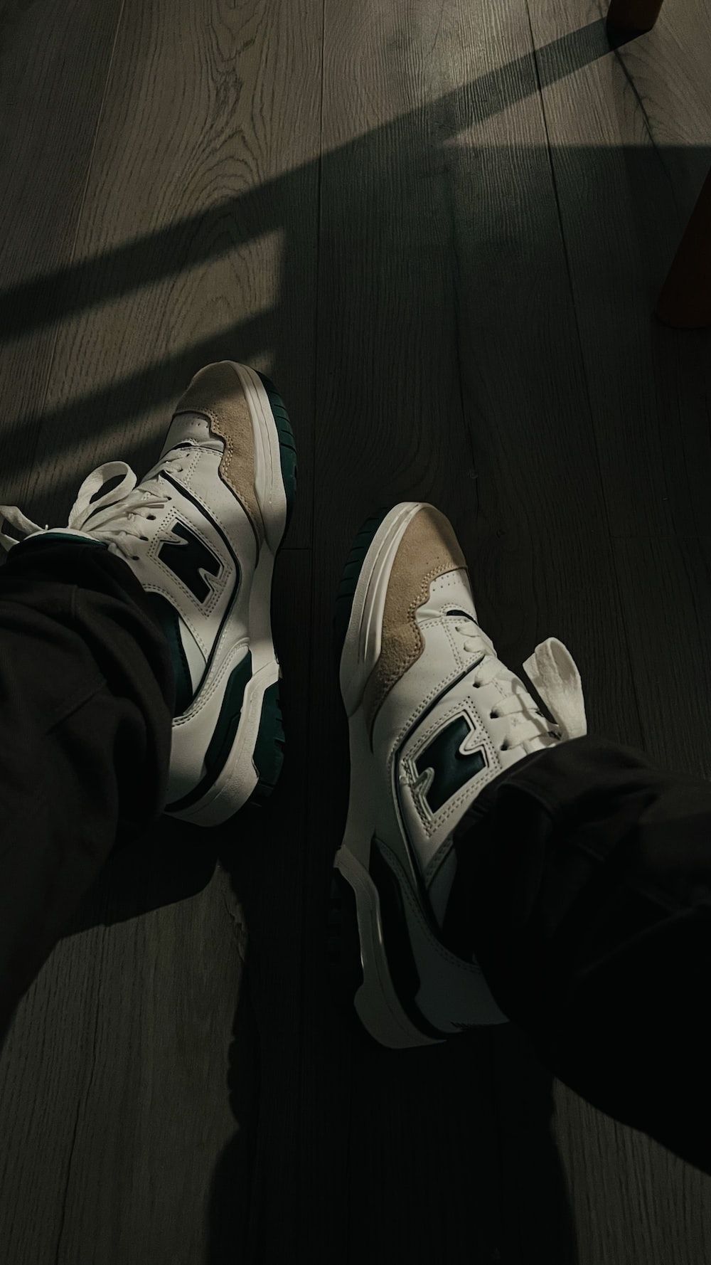 A pair of feet wearing sneakers standing on a wooden floor. - Air Jordan