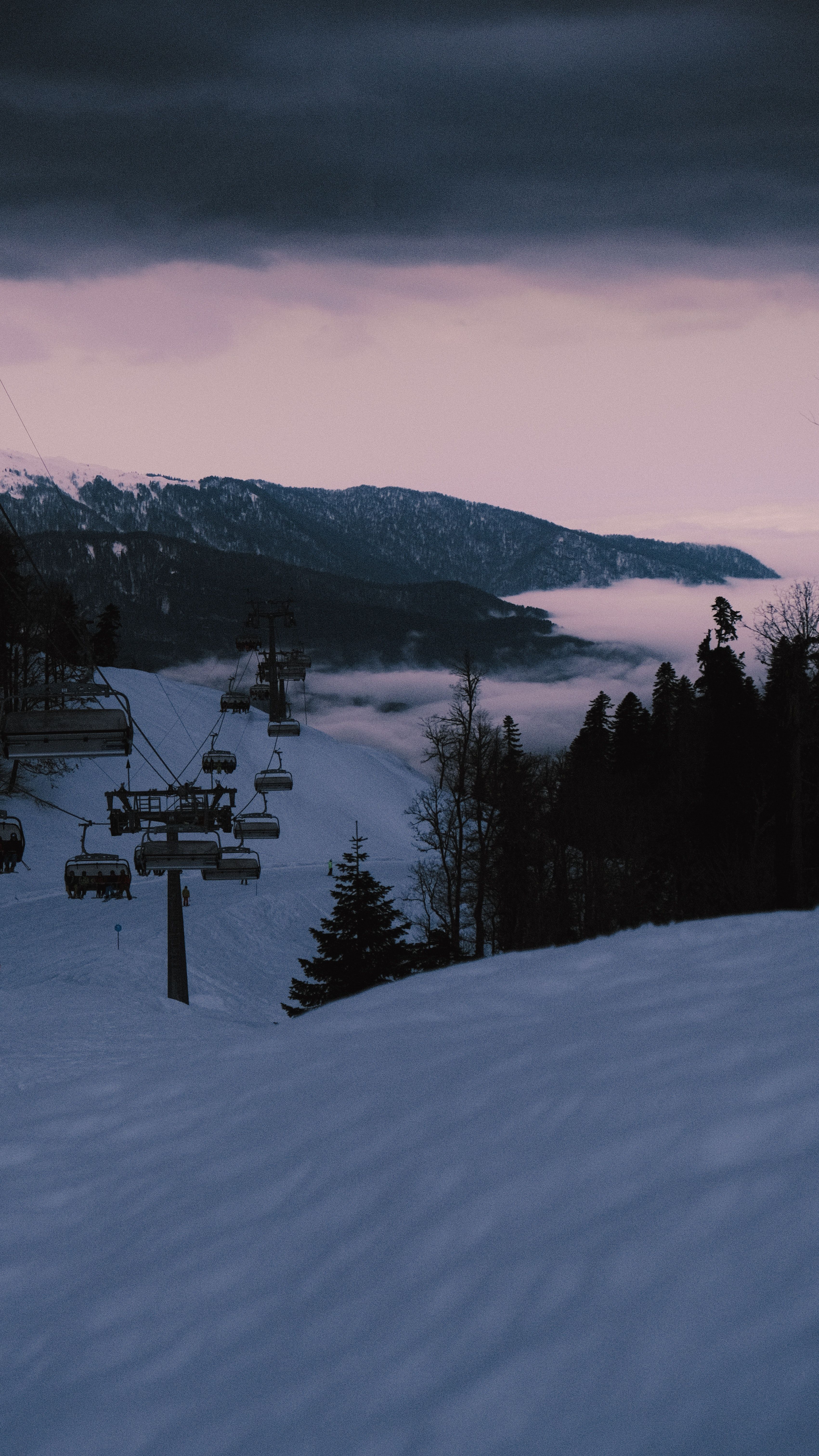 A ski lift is seen at dusk in the snow. - Ski