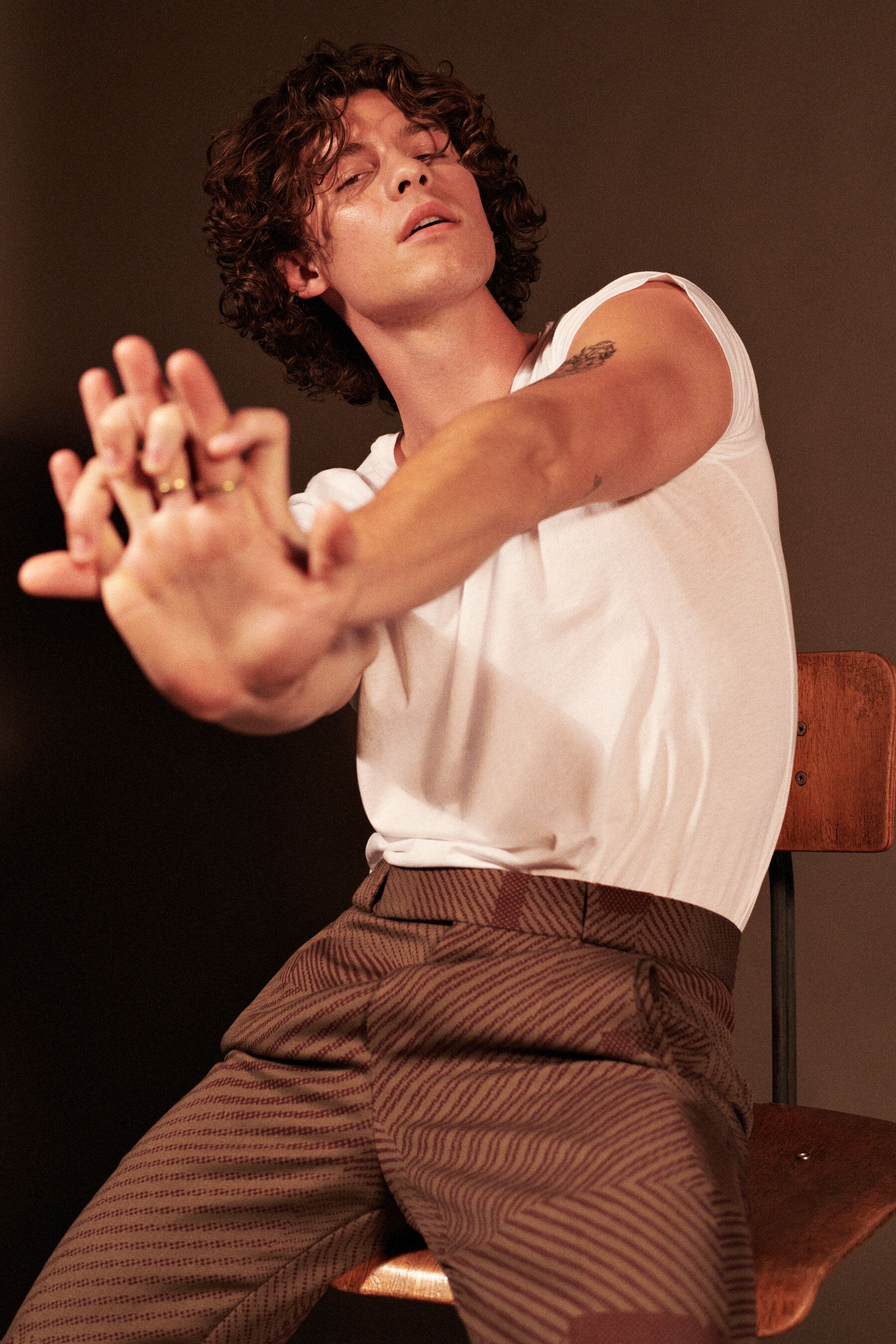 Shawn Mendes sitting on a chair wearing a white shirt and brown pants - Shawn Mendes