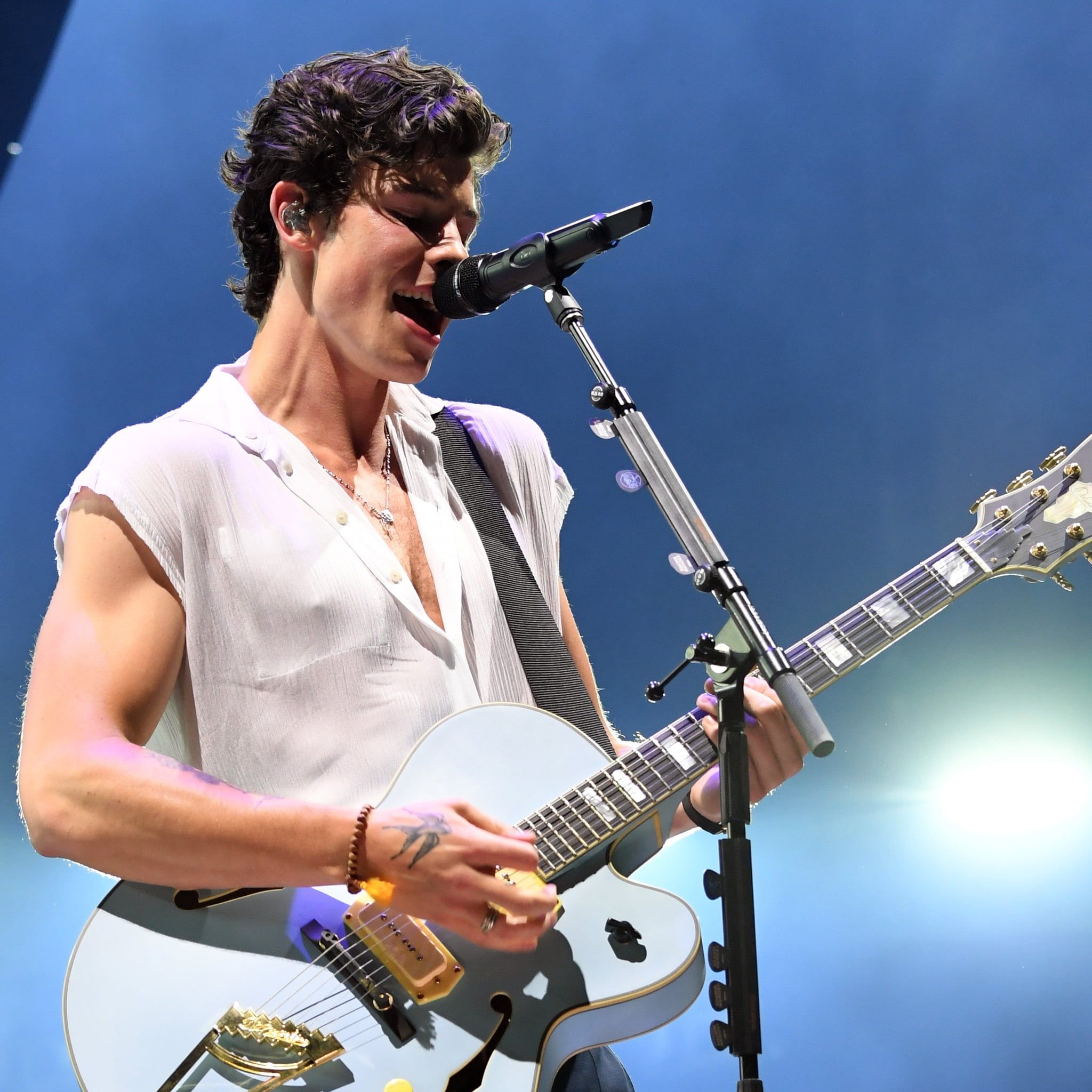 A man singing into the microphone while playing guitar - Shawn Mendes