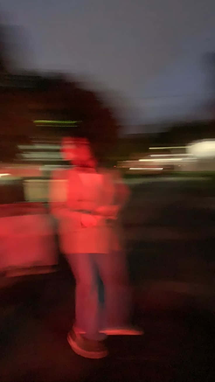 A blurry image of a person in a red jacket standing in front of a truck. - Blurry