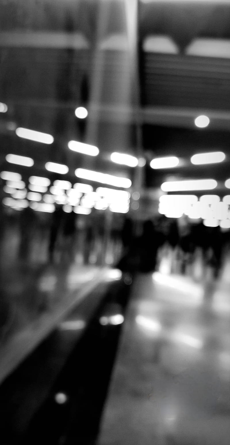 A black and white photo of a subway station with people walking in the background. - Blurry