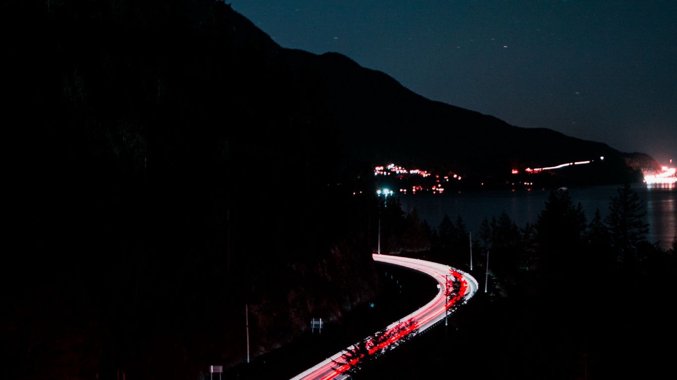 A long exposure photo of a highway at night with cars moving in a line. - 1366x768, road