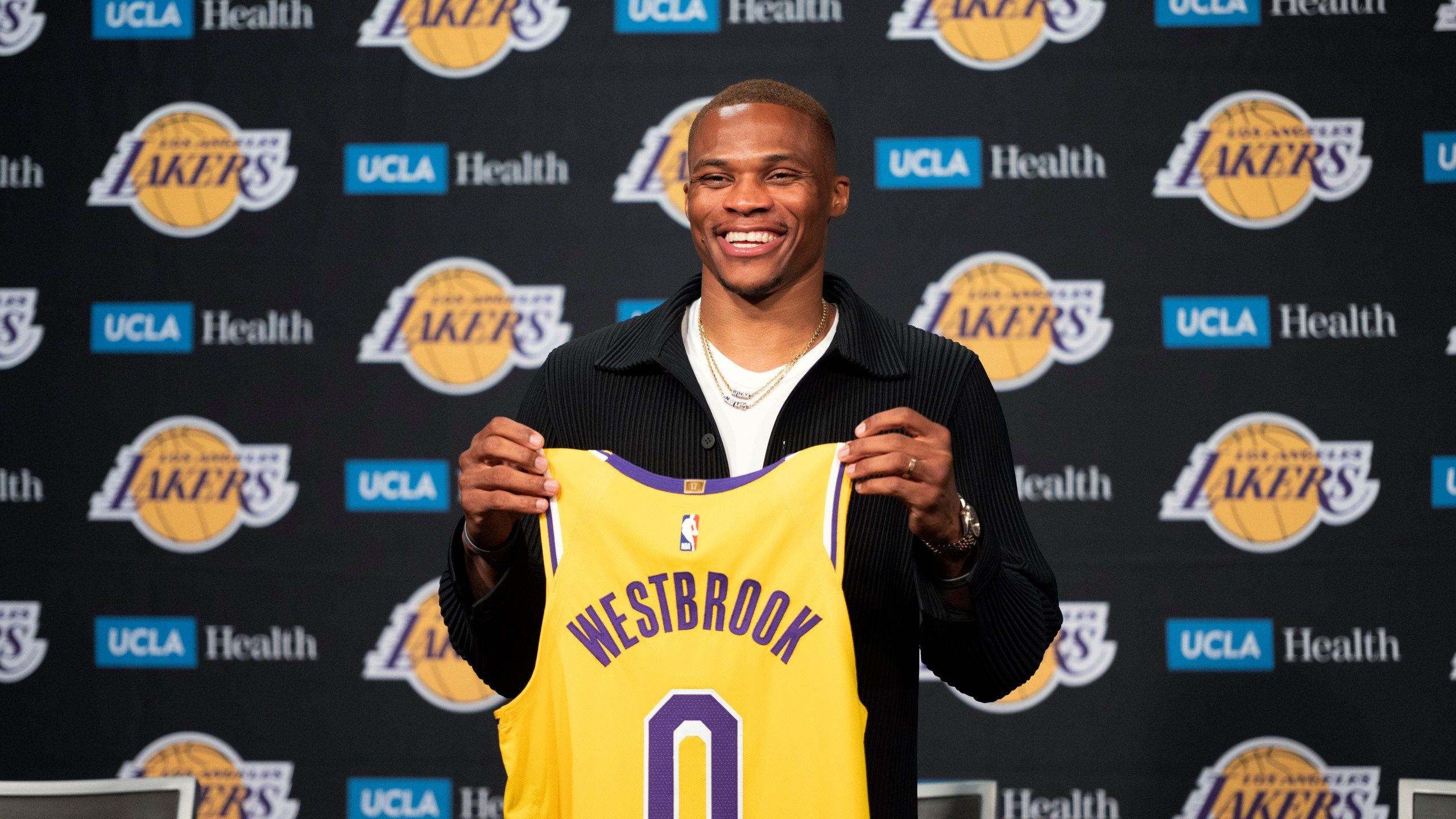 Russell Westbrook smiles as he holds up his Lakers jersey. - Los Angeles Lakers