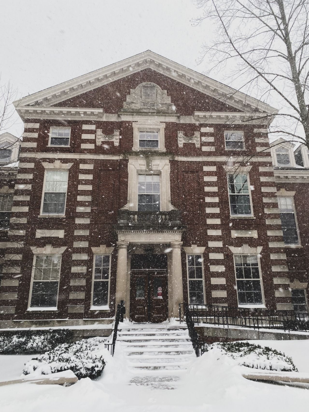 A red brick building with white trim and columns in the snow. - Harvard