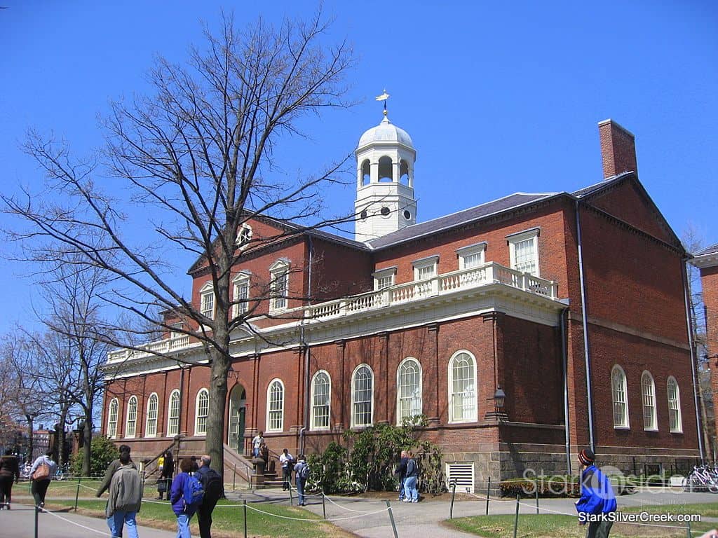 Students walking on a sidewalk in front of a large brick building. - Harvard