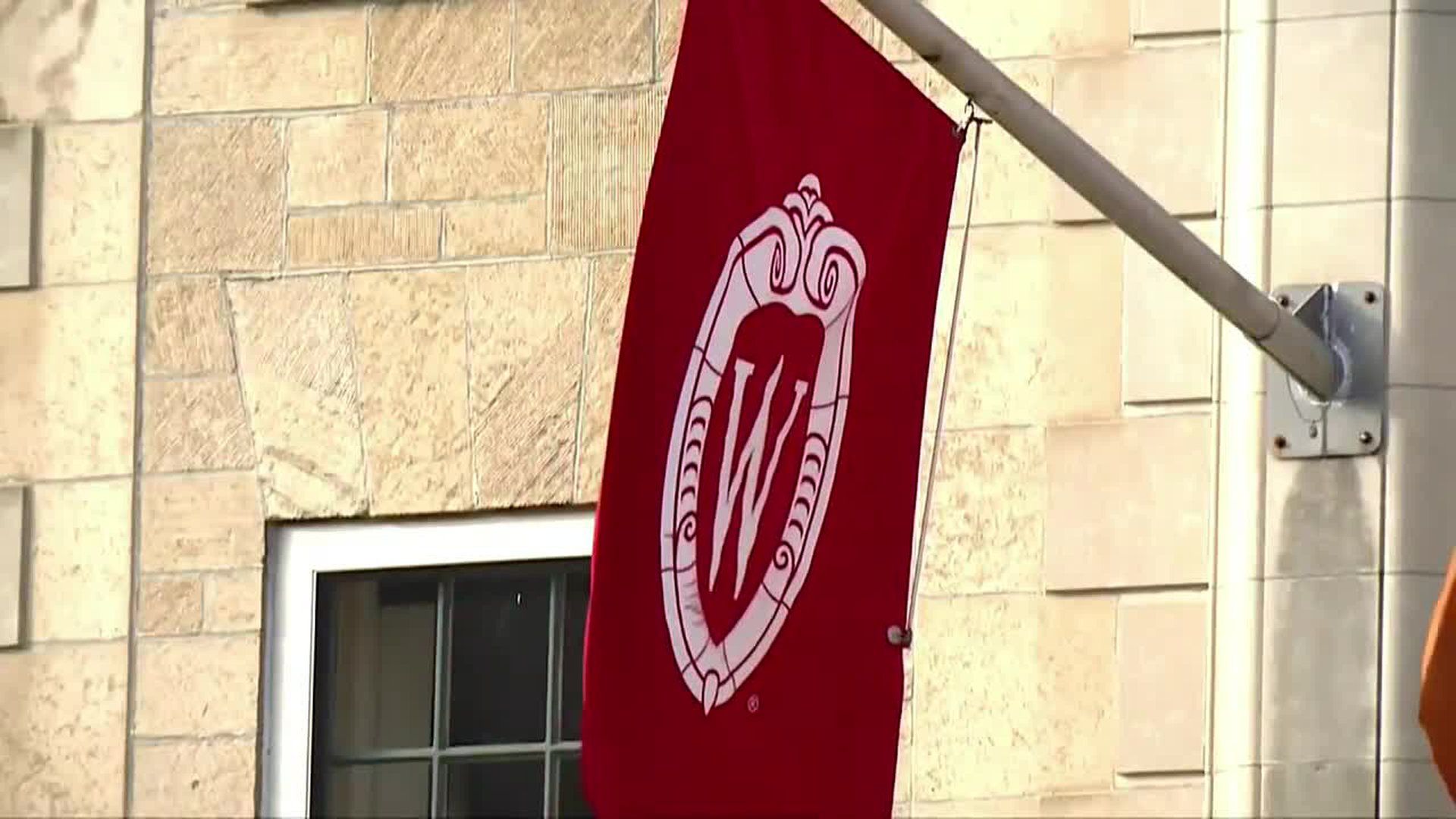 A red flag with the University of Wisconsin-Madison crest is hanging from a flag pole. - Harvard