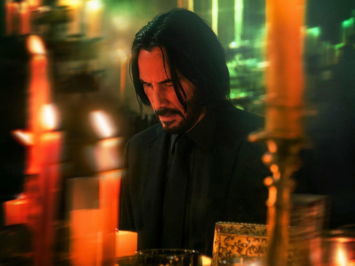 John Wick (Keanu Reeves) in a church, surrounded by candles, looking at a picture of his wife - John Wick