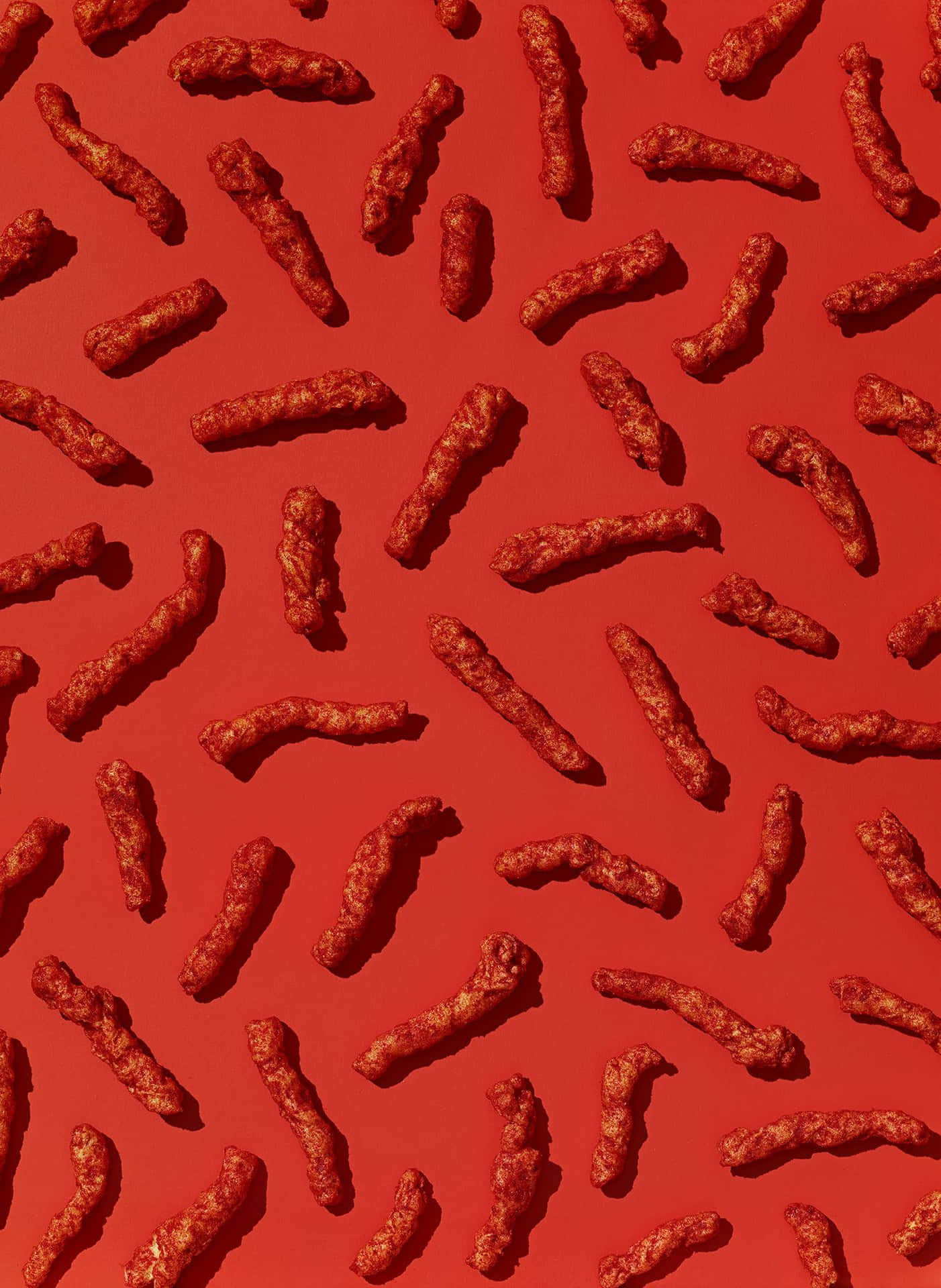 A red background with an array of red cheetos on it - Cheetos