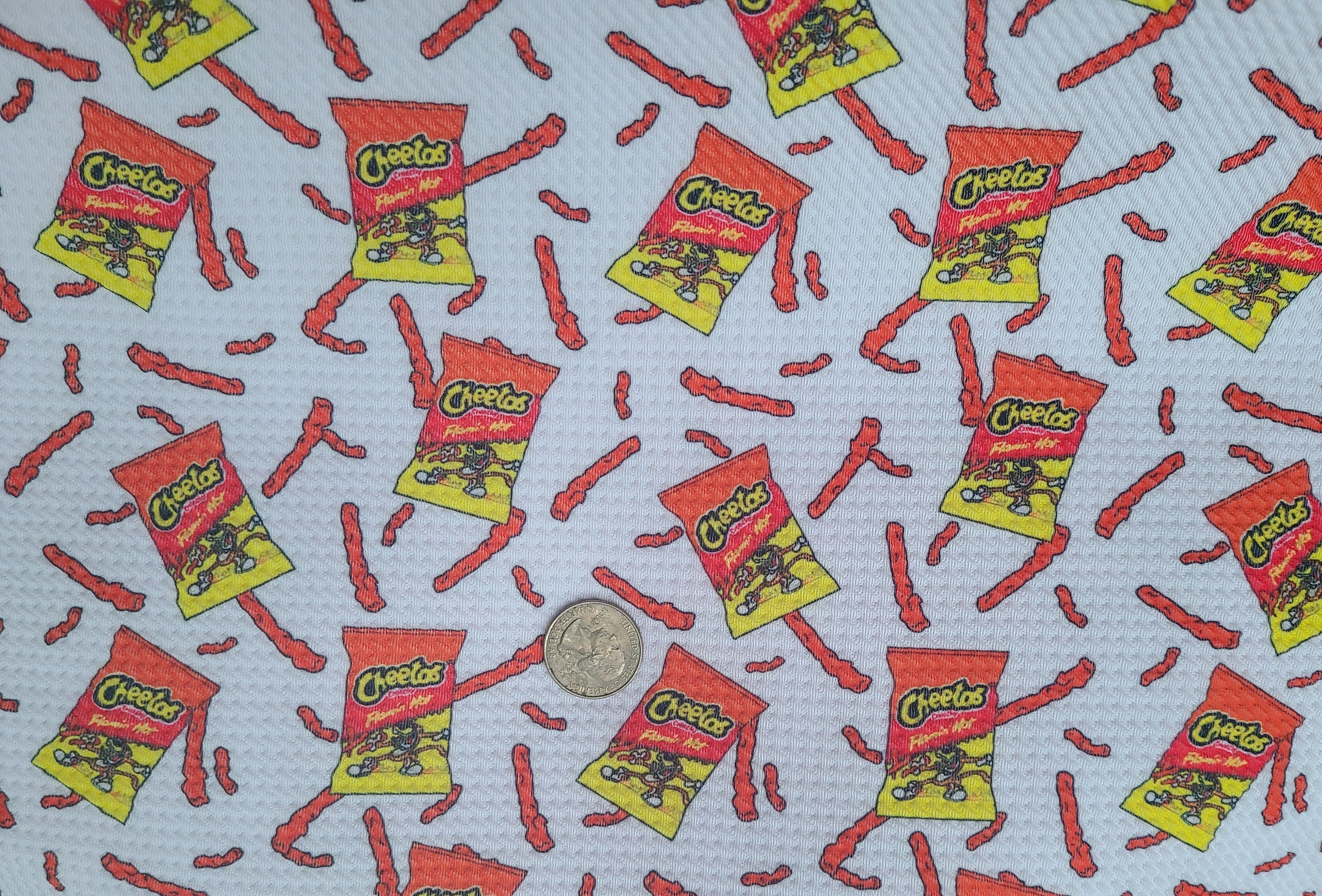 A white piece of fabric with red and yellow cheetos and cheetos packets on it. - Cheetos