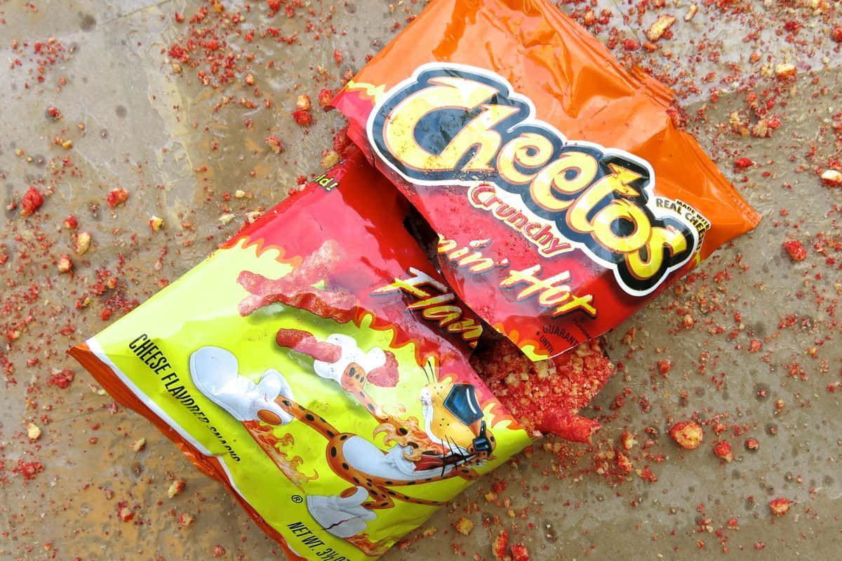 Two bags of Cheetos Puffs, one red and one orange, are open and spilled out on a concrete surface. - Cheetos