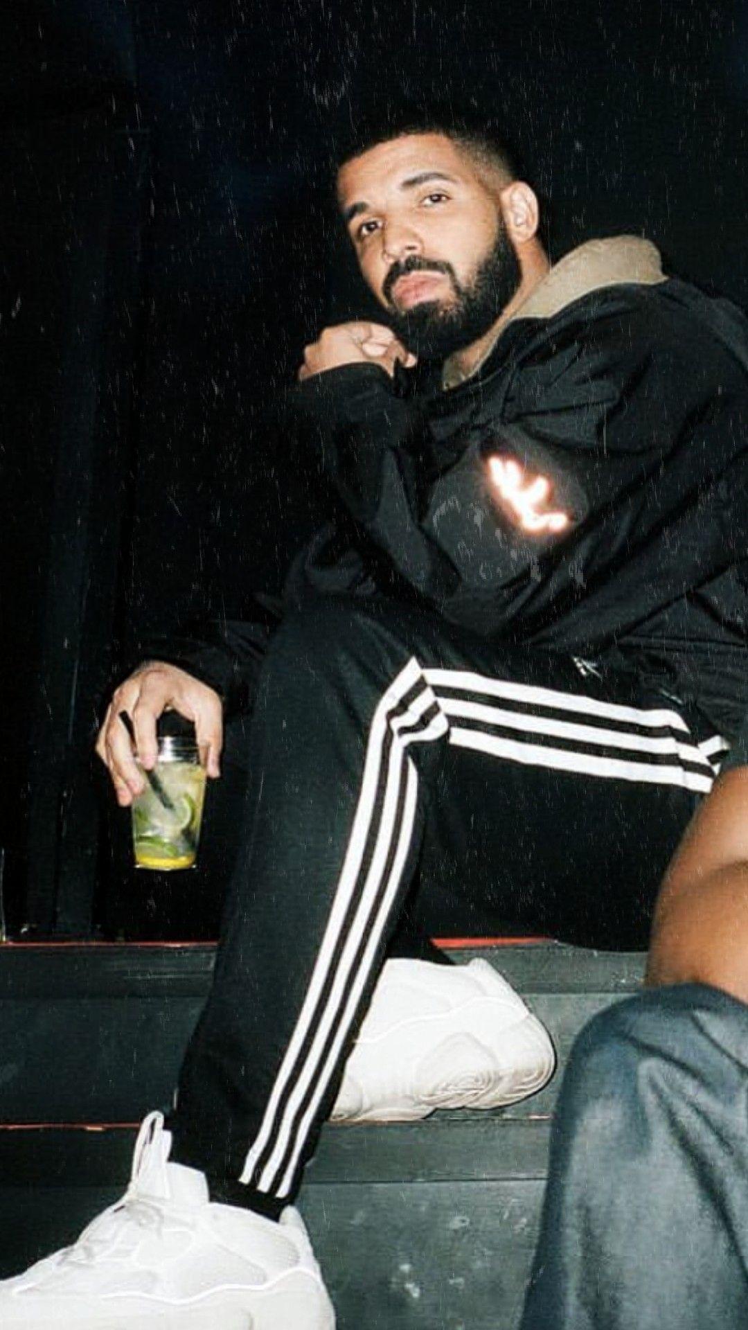 Rapper Drake sitting on a step holding a drink - Drake