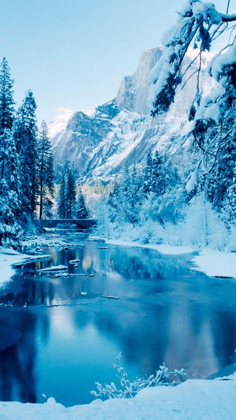 A frozen river surrounded by snow covered trees and mountains - Winter, river