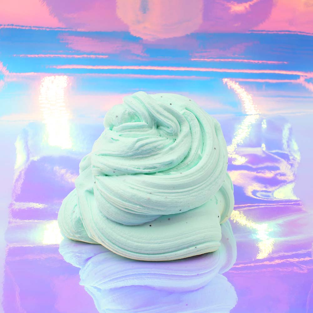 A stack of minty green fluffy slime sits on a reflective surface with a pastel sky in the background. - Slime