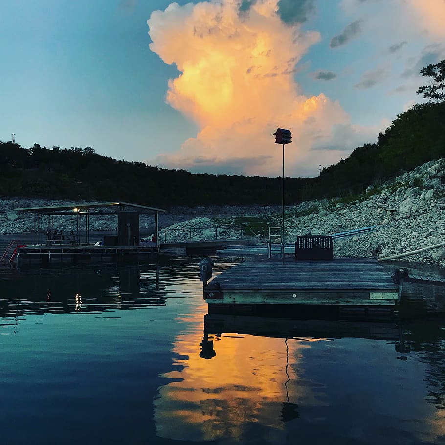 A dock sits on the water with a large cloud in the sky. - Lake
