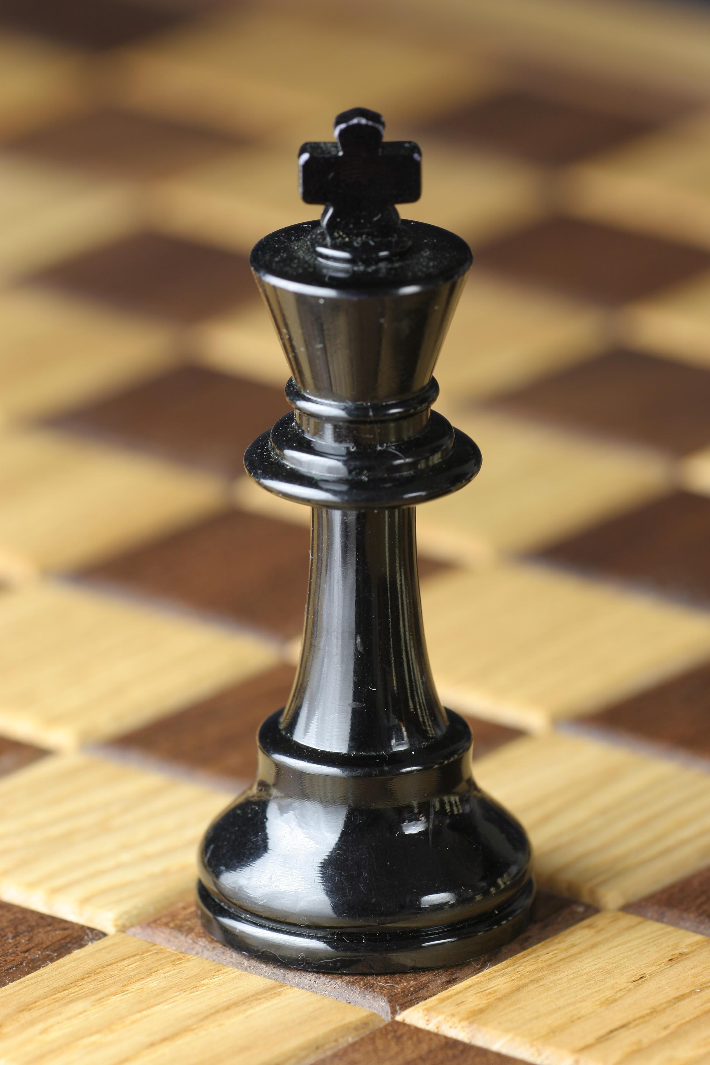 A black king chess piece on a wooden chess board - Chess