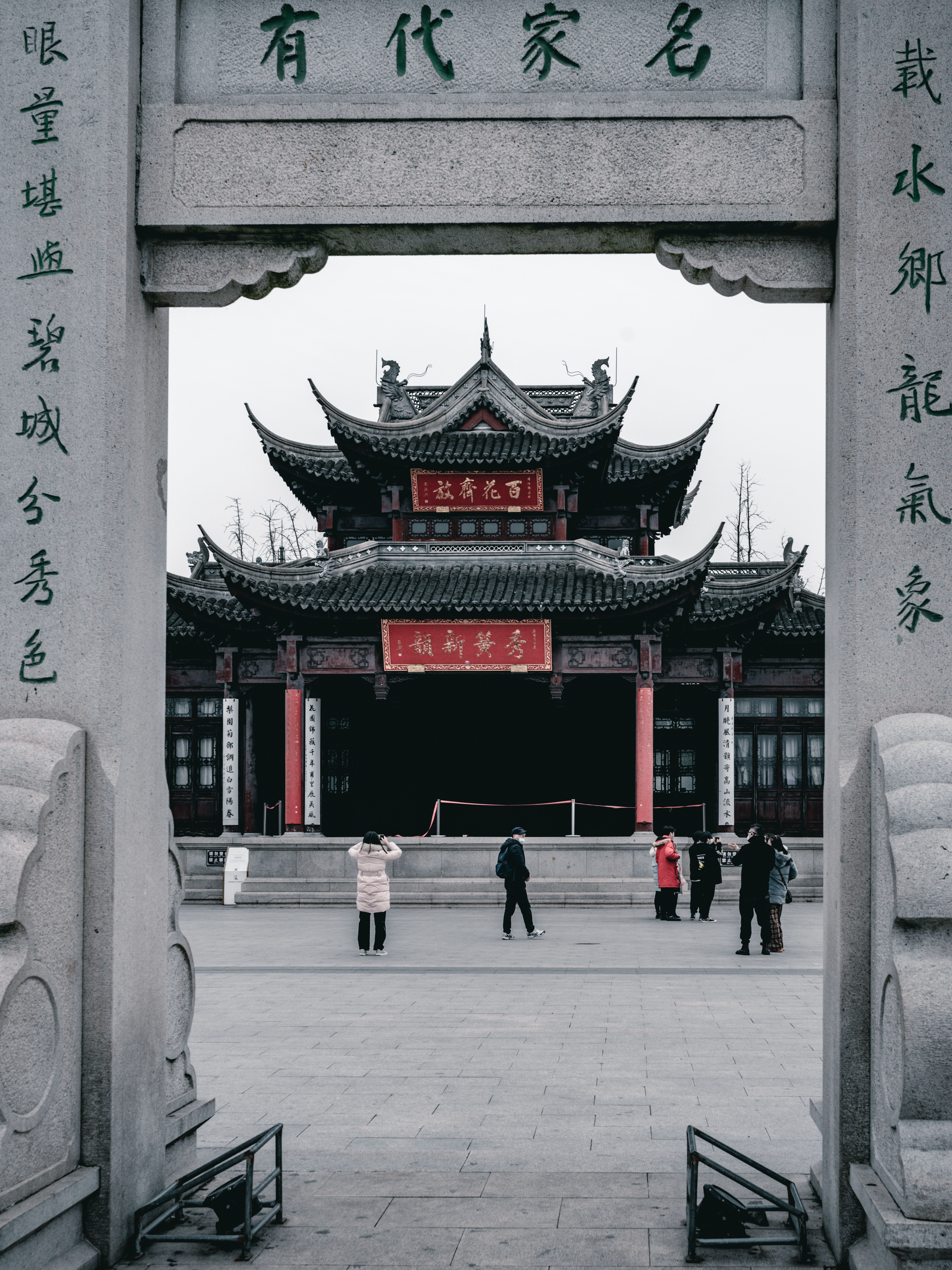 The front of a Chinese building with arches and people walking around. - Chinese