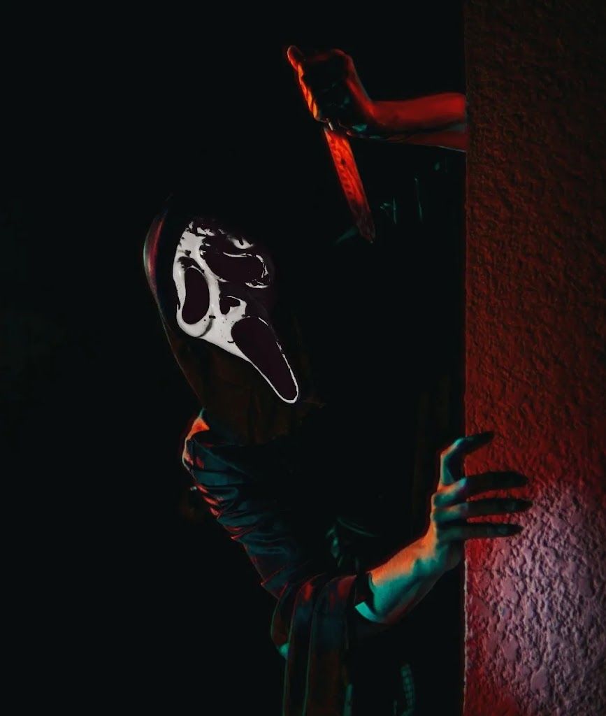 A person in a scream mask crouching in the dark - Ghostface