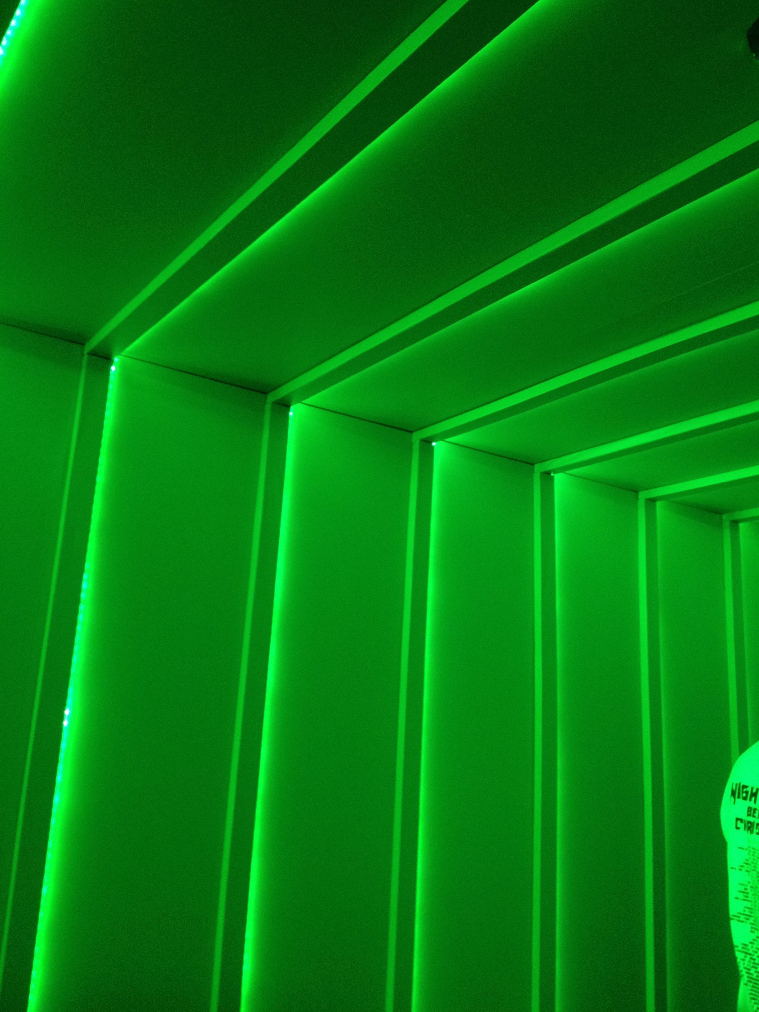 A green-lit wall with ridges and a person's arm in the corner. - Neon green