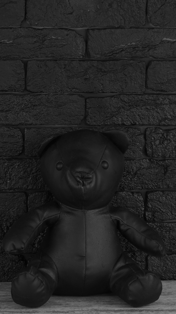 A black teddy bear is placed against a black brick wall. - Teddy bear, emo