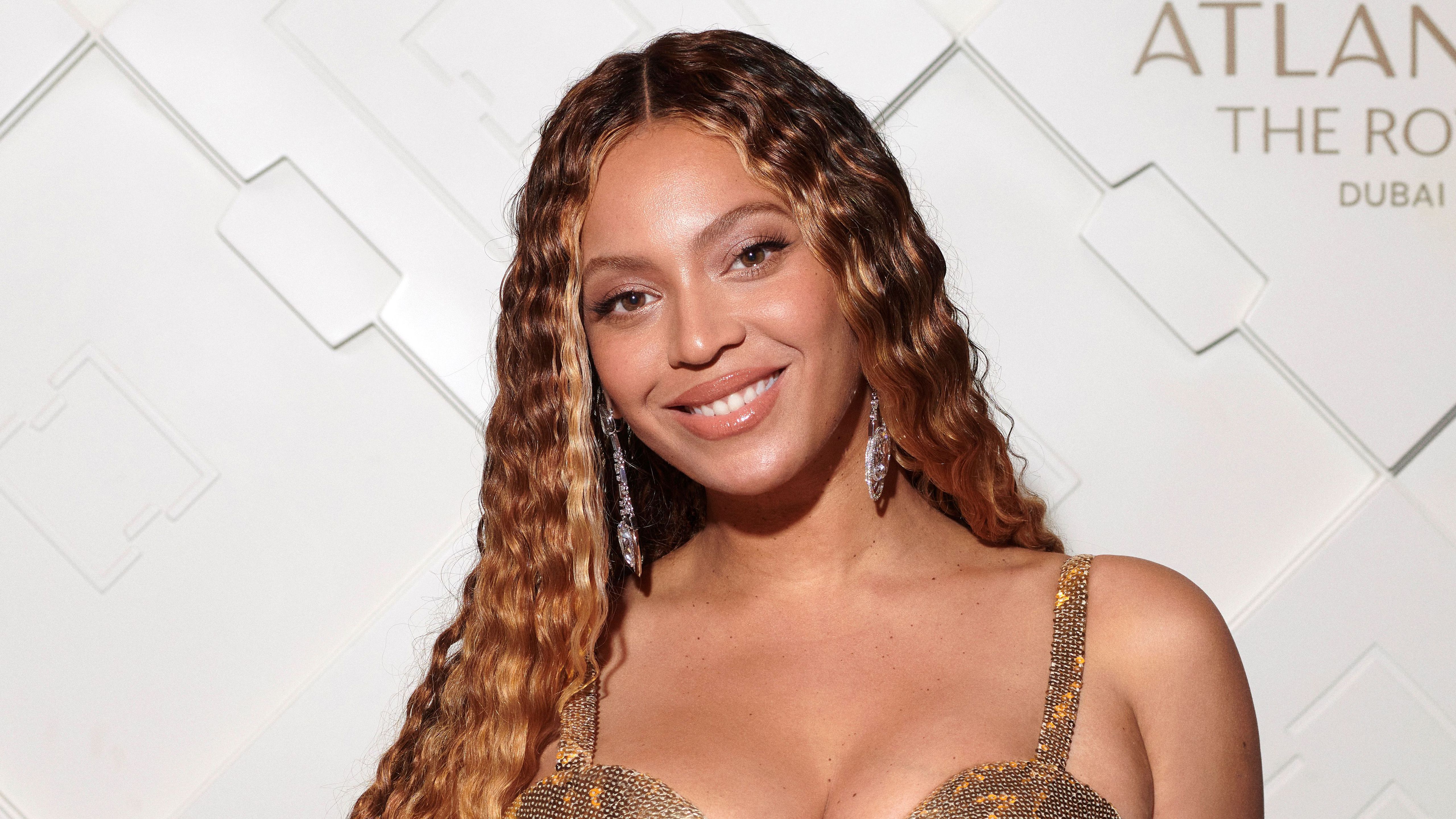 Beyoncé wears a gold dress and long curly hair and smiles at the camera - Beyonce