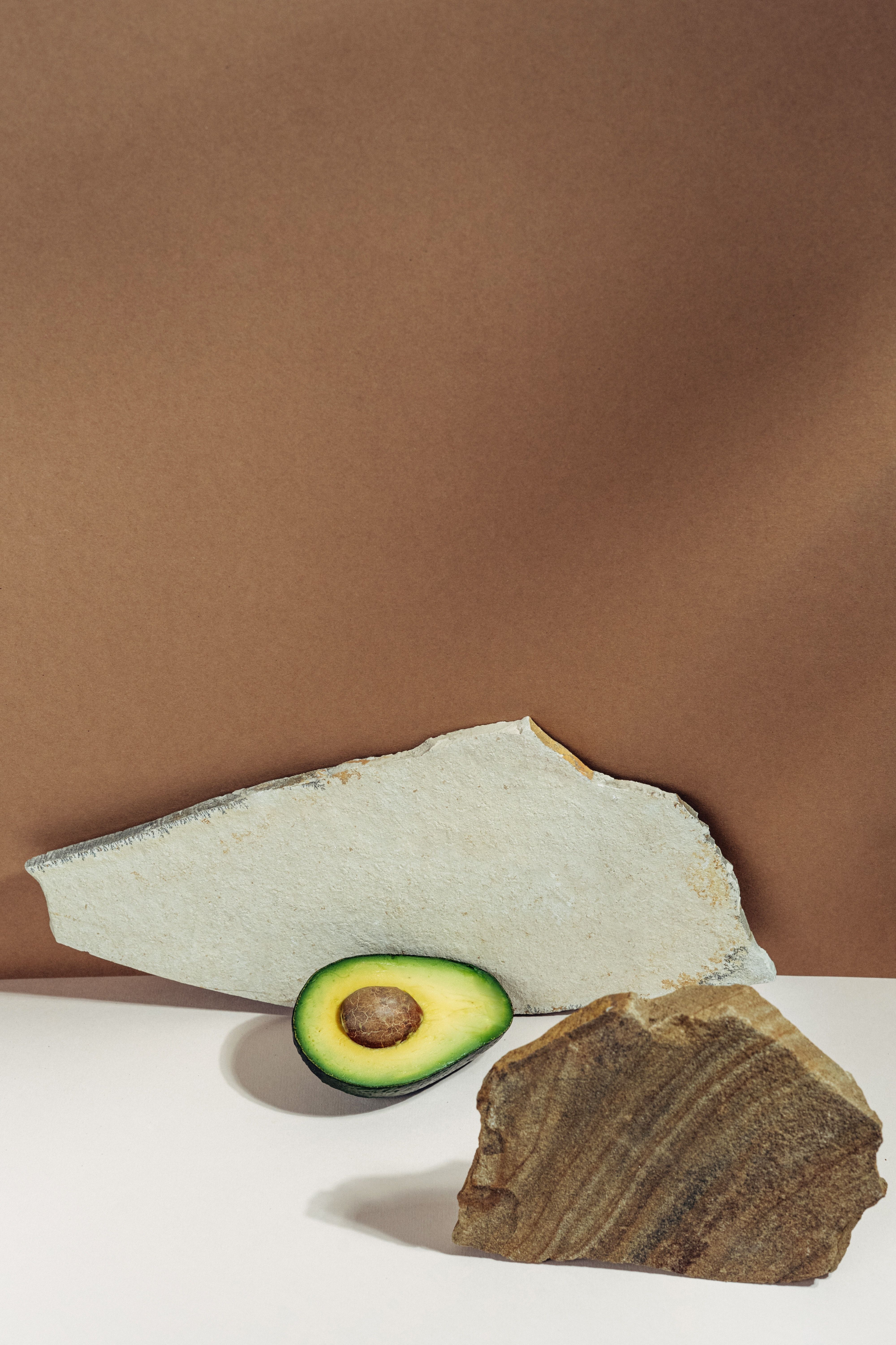 A sliced avocado on a white surface with a brown background. - Avocado