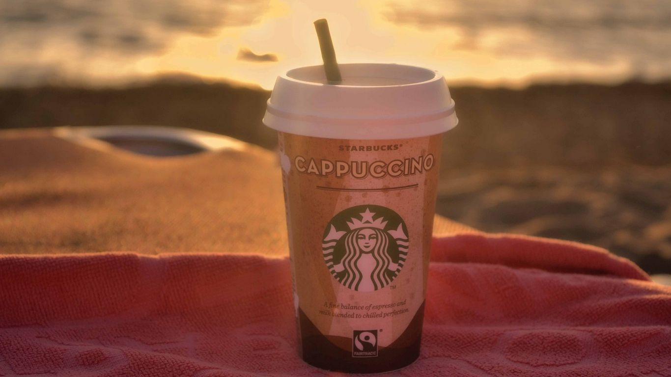 A Starbucks cup with a straw sits on a blanket. - Starbucks