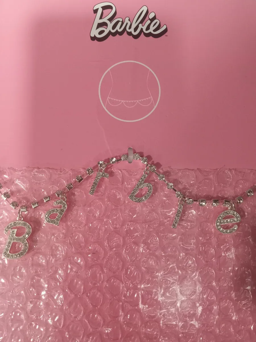 A silver Barbie belly chain with rhinestones on a pink background. - Barbie