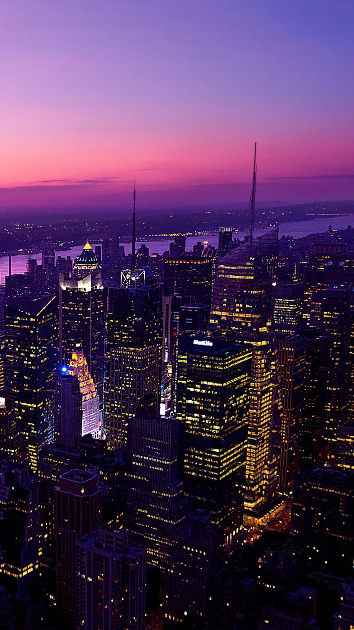 A city skyline at night with skyscrapers lit up in purple and pink hues. - New York