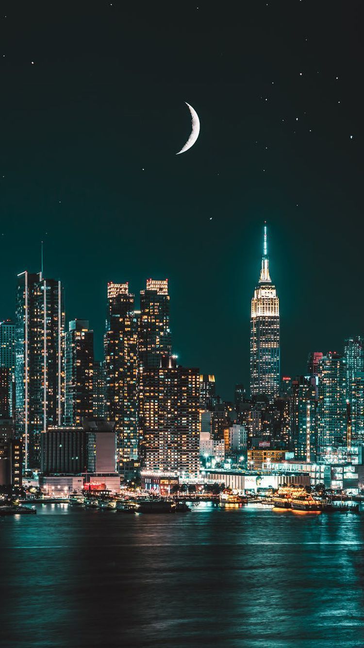 A cityscape lit up at night with a sliver of moon in the sky - New York