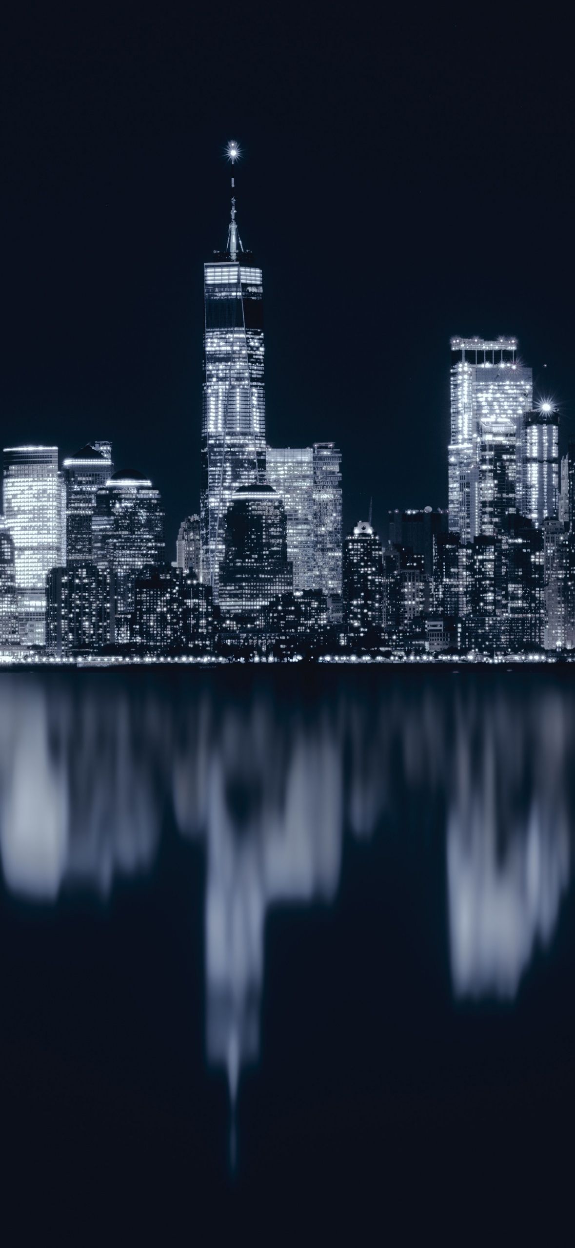 The skyline of a city at night with a reflection in the water. - New York, cityscape