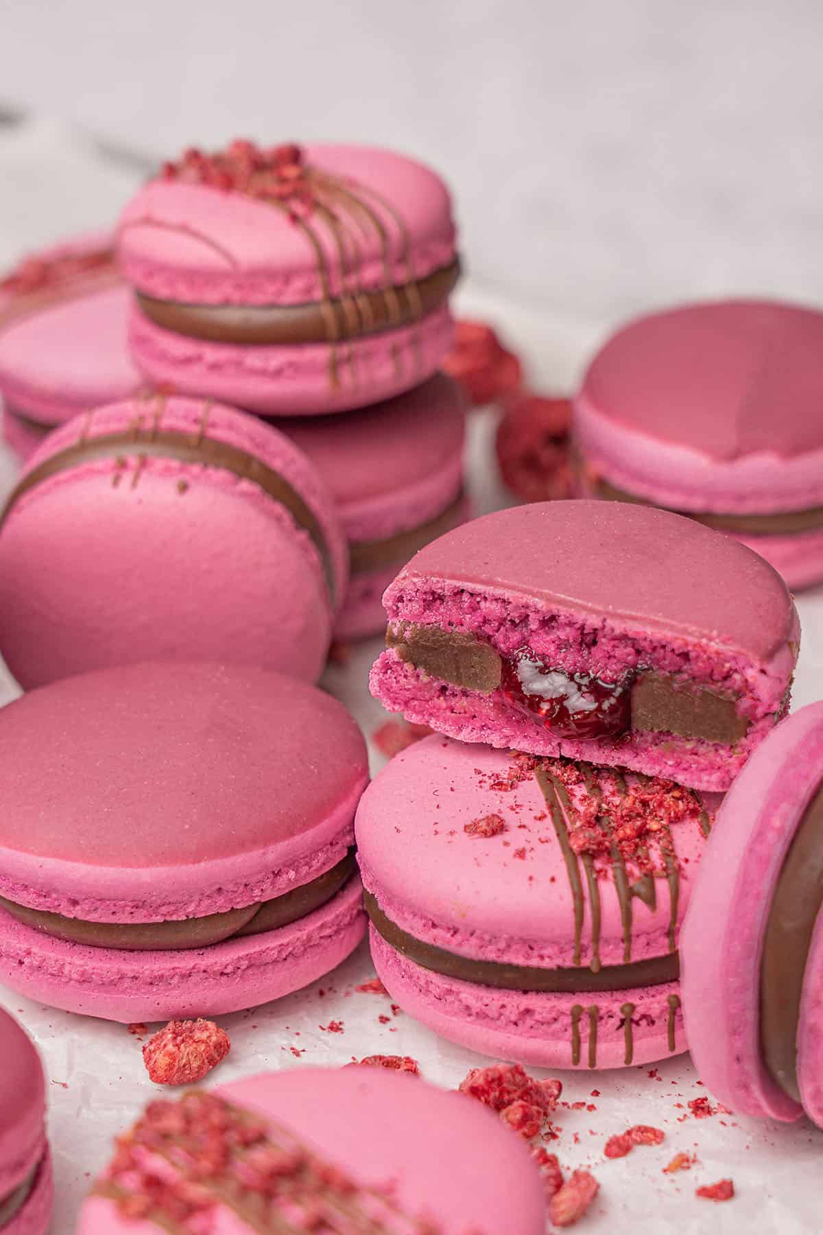 Raspberry white chocolate macarons with a chocolate filling, some of them are halved to show the inside. - Macarons