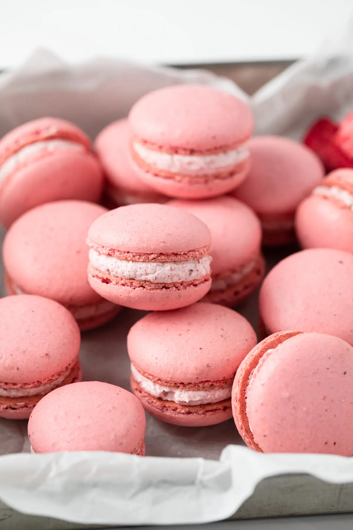 A plate of pink macarons with a white filling. - Macarons, bakery