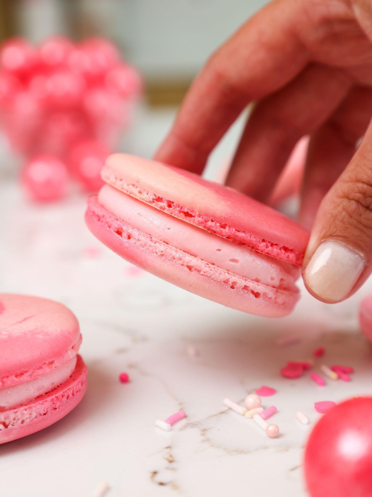 A person holding a pink macaron in their hand. - Macarons