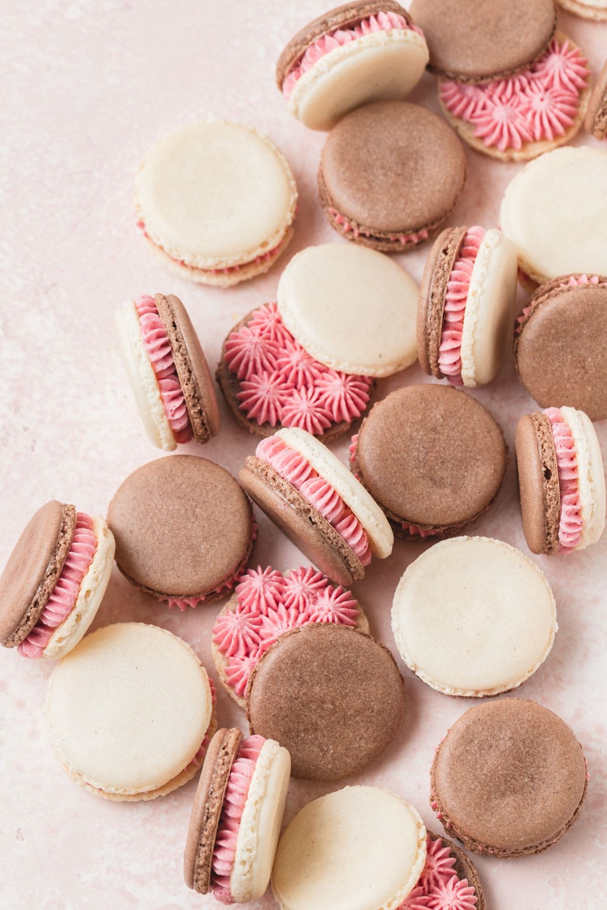 A plate of chocolate and vanilla macarons with pink frosting in the middle. - Macarons