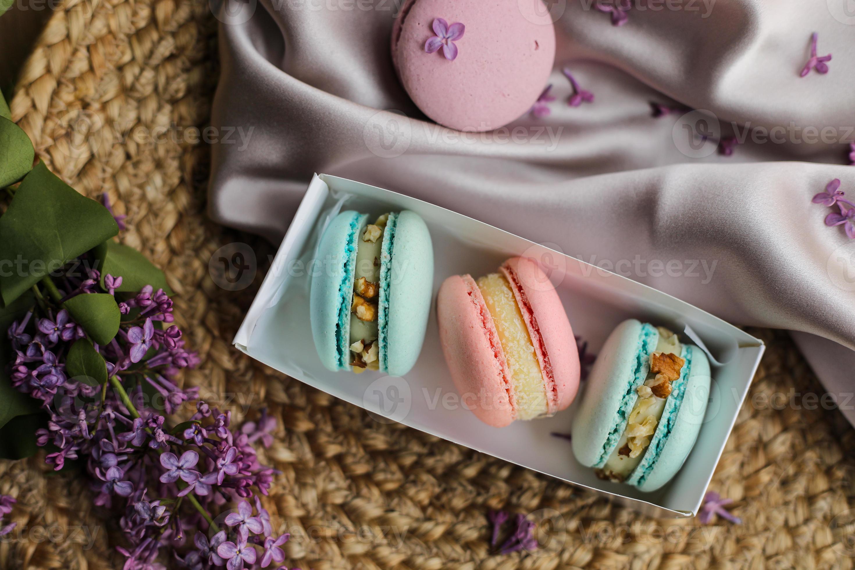 pink and mint french macaroons or macarons cookies in gift box and a lilac flowers on a cloth and straw stand background. Natural fruit and berry flavors, creamy stuffing for valentines, mother day