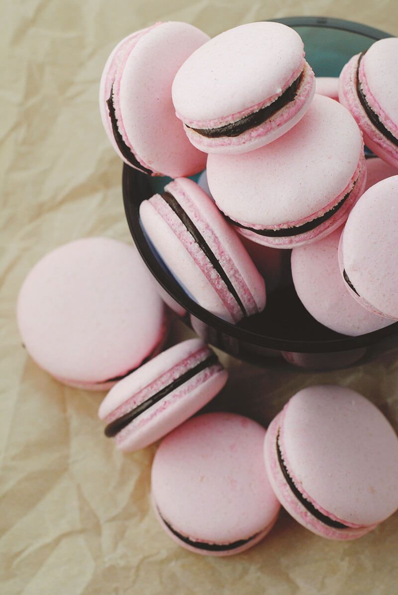 A bowl of pink macaroons with chocolate filling. - Macarons