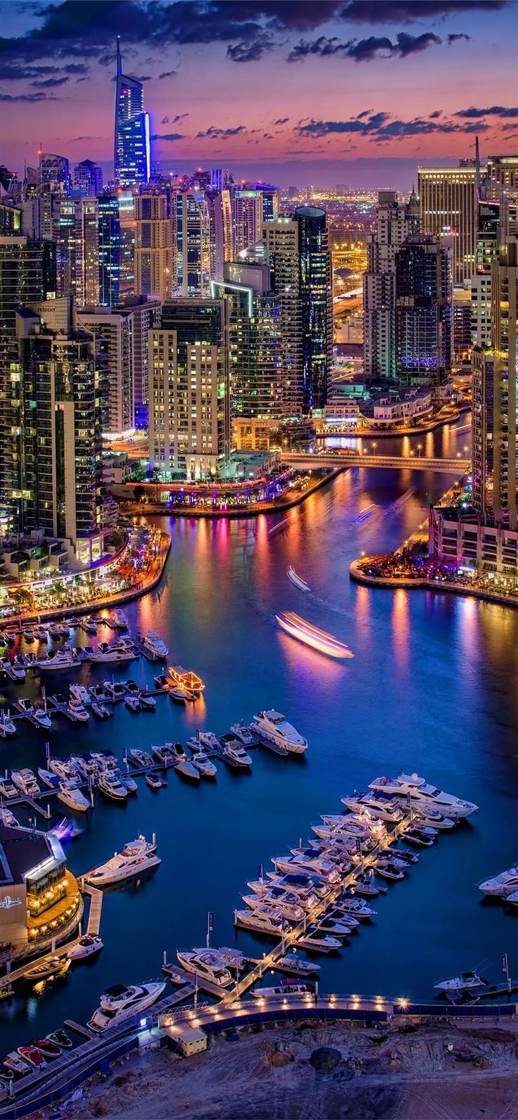 Boats are docked in the harbor at night. - Dubai