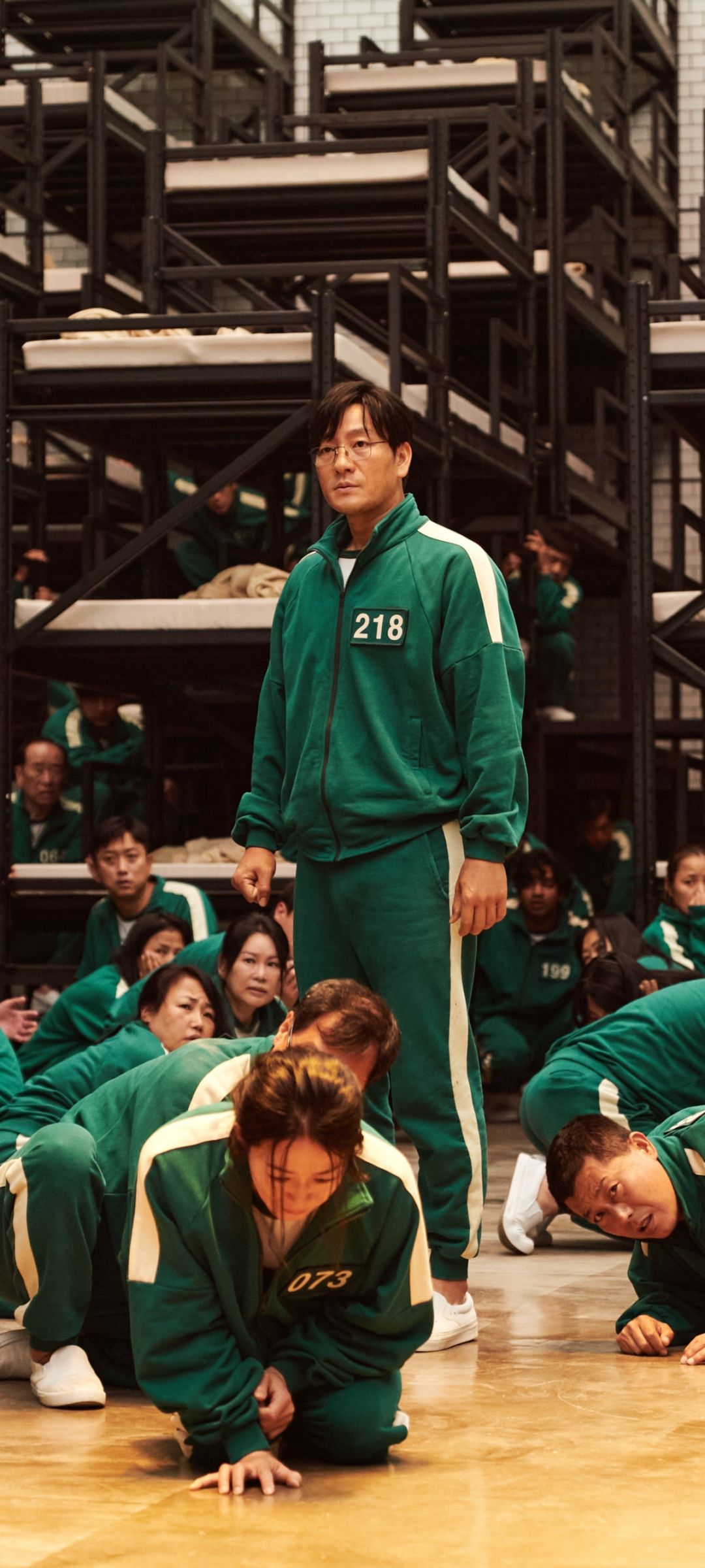 A still from the movie 'Parasite'. A man stands in front of a group of people in matching green tracksuits. - Squid Game