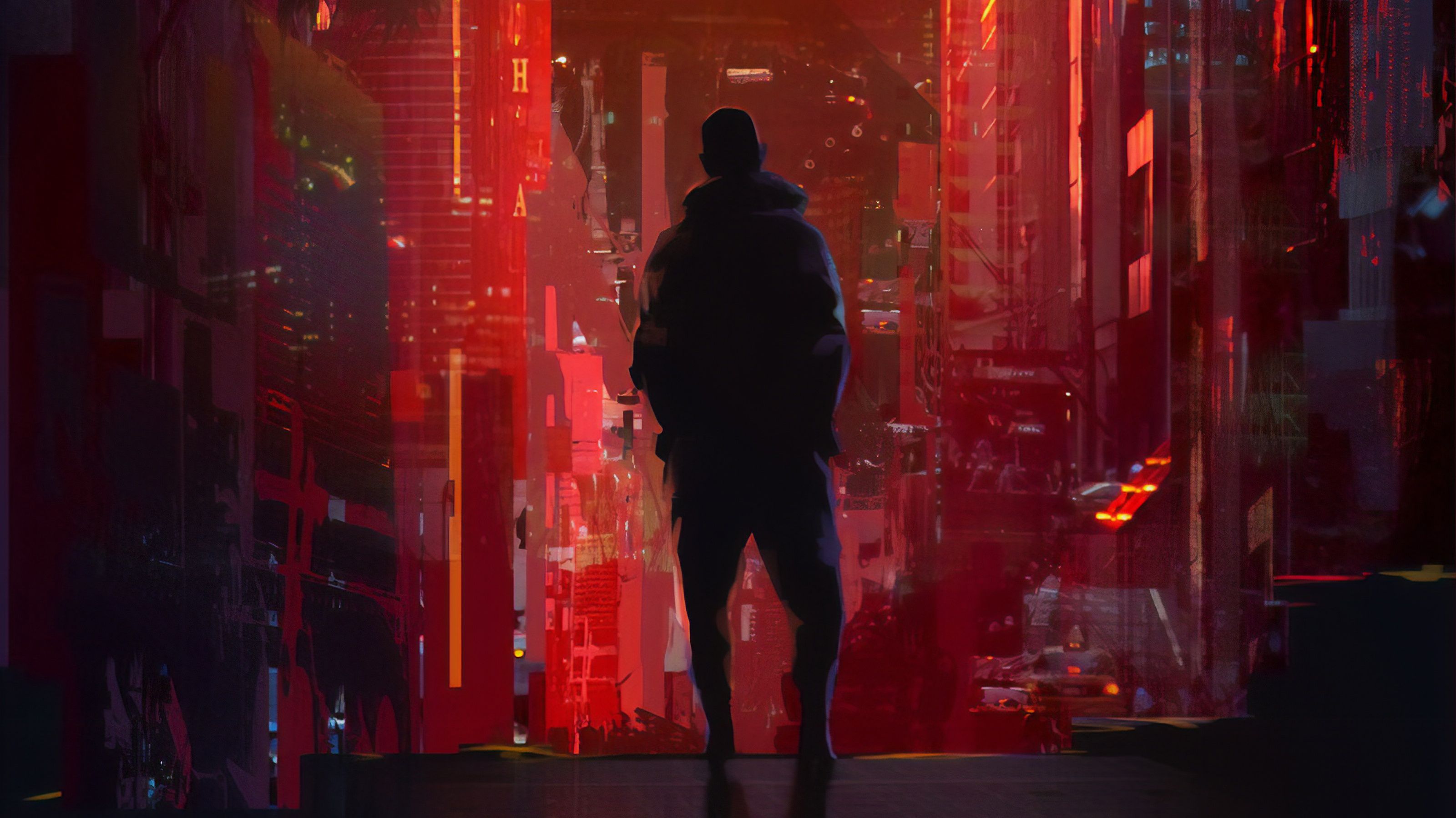 A man in a black hoody stands in a red-lit city street - California