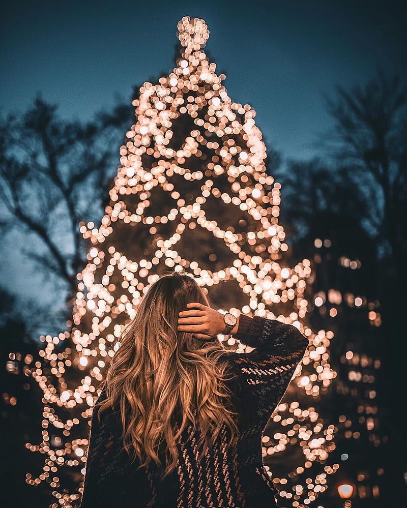 A woman standing in front of a Christmas tree with lights. - Christmas lights