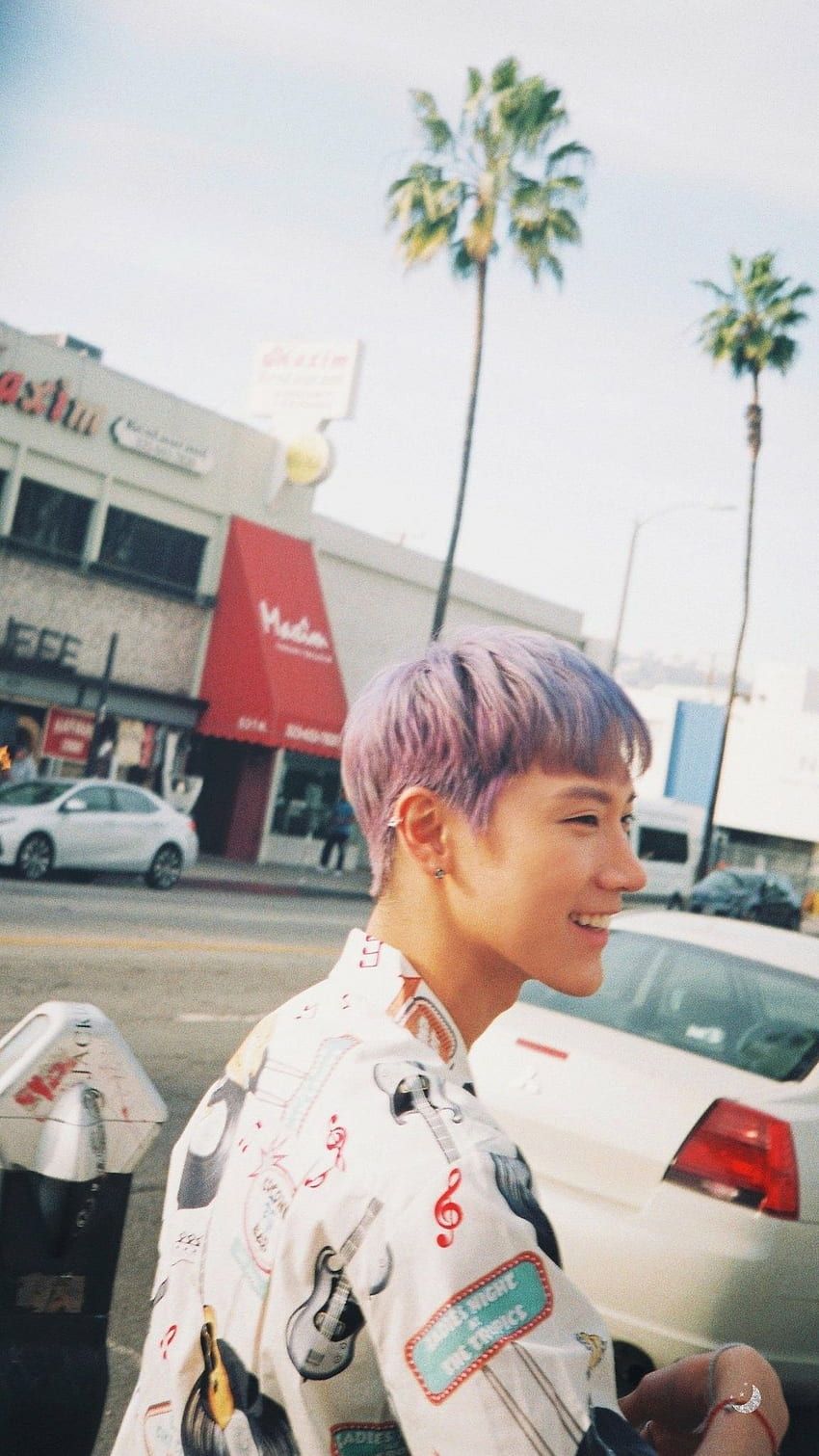 A person with purple hair standing in front of a building. - NCT