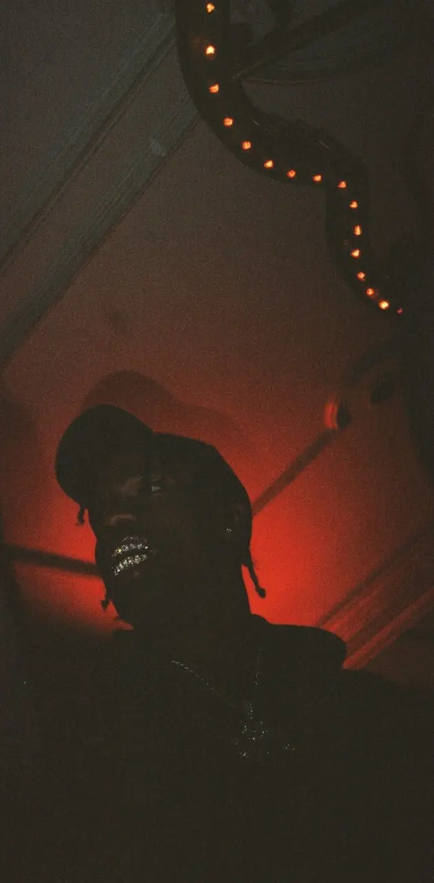 A man in a hat and jacket standing under a red light. - Travis Scott
