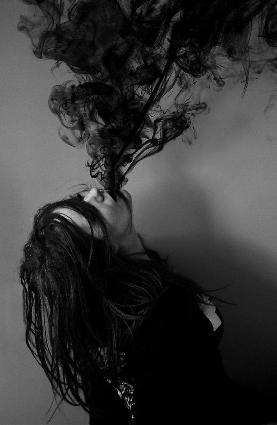 A woman with black hair and black clothes exhales black smoke. - Smoke