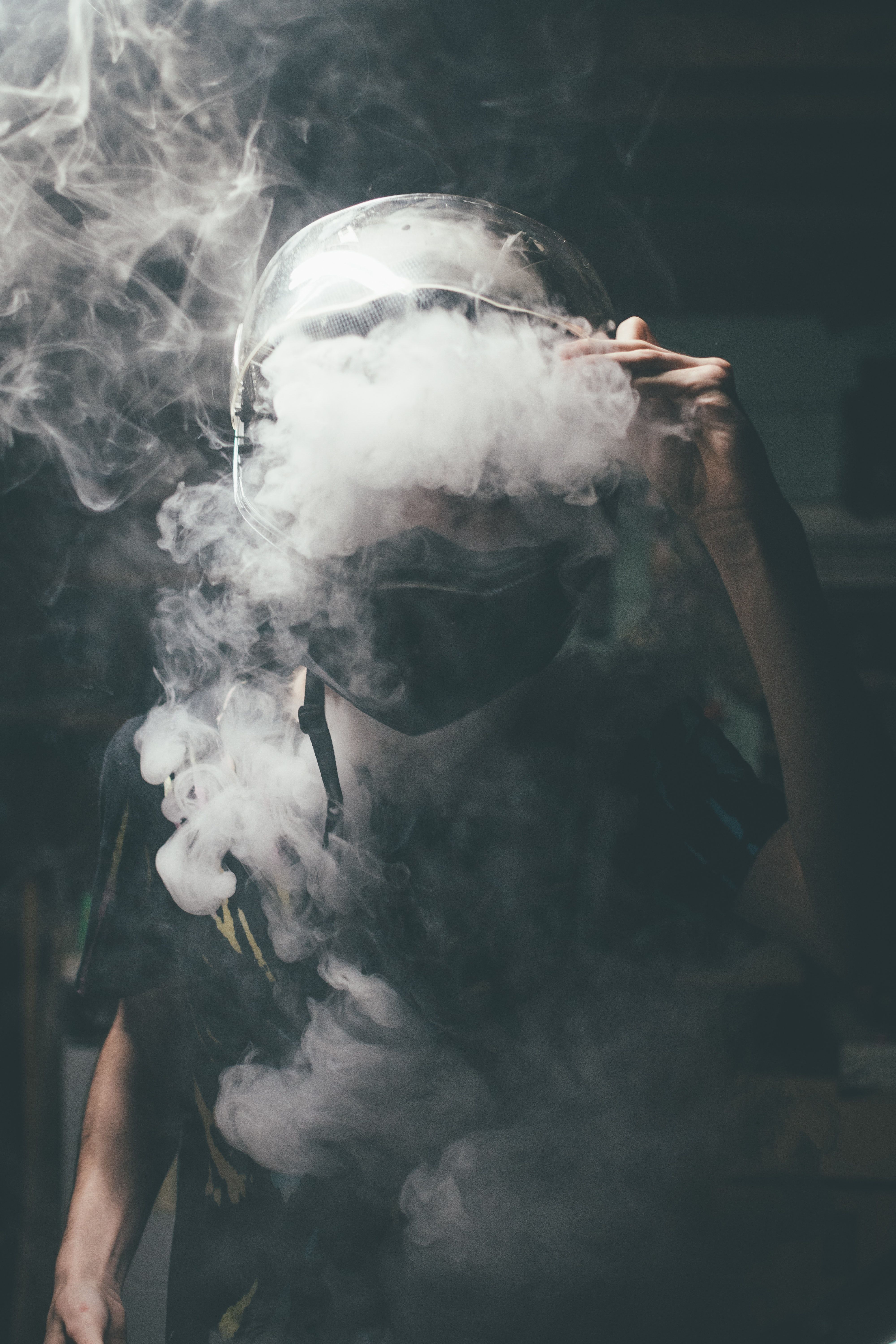 A man wearing a motorcycle helmet and goggles is surrounded by smoke. - Smoke