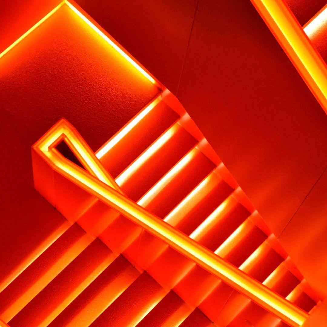 A photograph of a staircase with neon orange lighting. - Neon orange