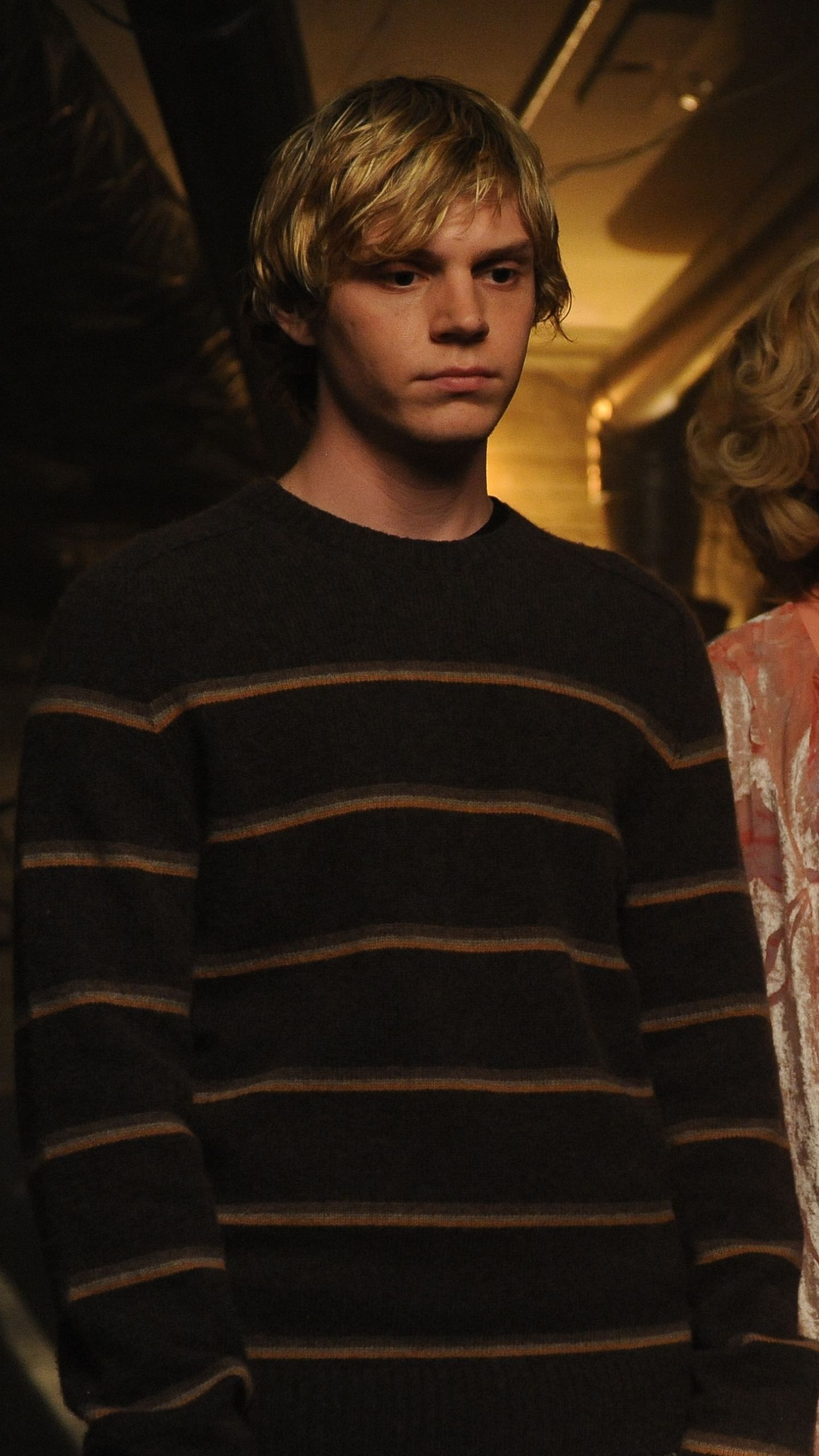 Evan Peters as Tate in American Horror Story: Hotel. Tate is wearing a striped sweater and looking off to the side. - Evan Peters