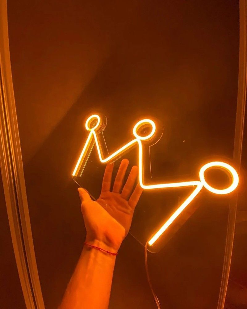 A hand is shown in front of a mirror with a neon sign that spells out 