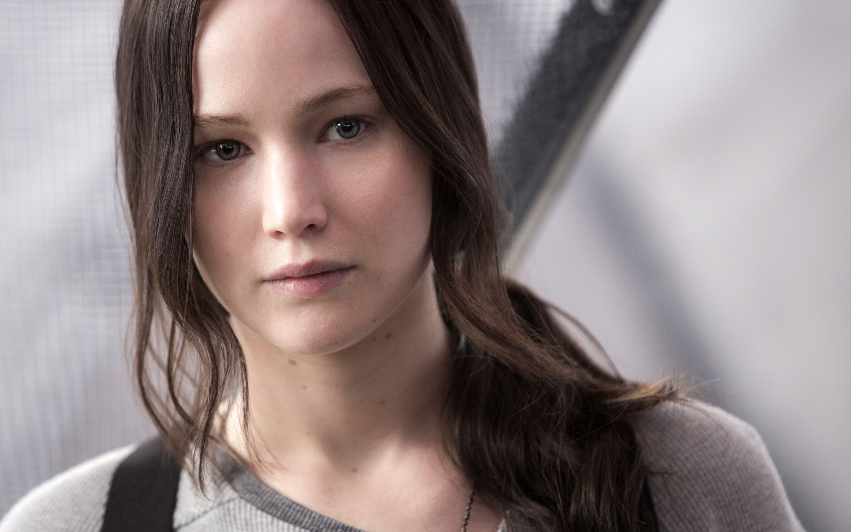 Jennifer Lawrence as Katniss Everdeen in The Hunger Games: Mockingjay Part 1. She's wearing a grey shirt and has a serious expression on her face. She's looking at the camera. - Jennifer Lawrence