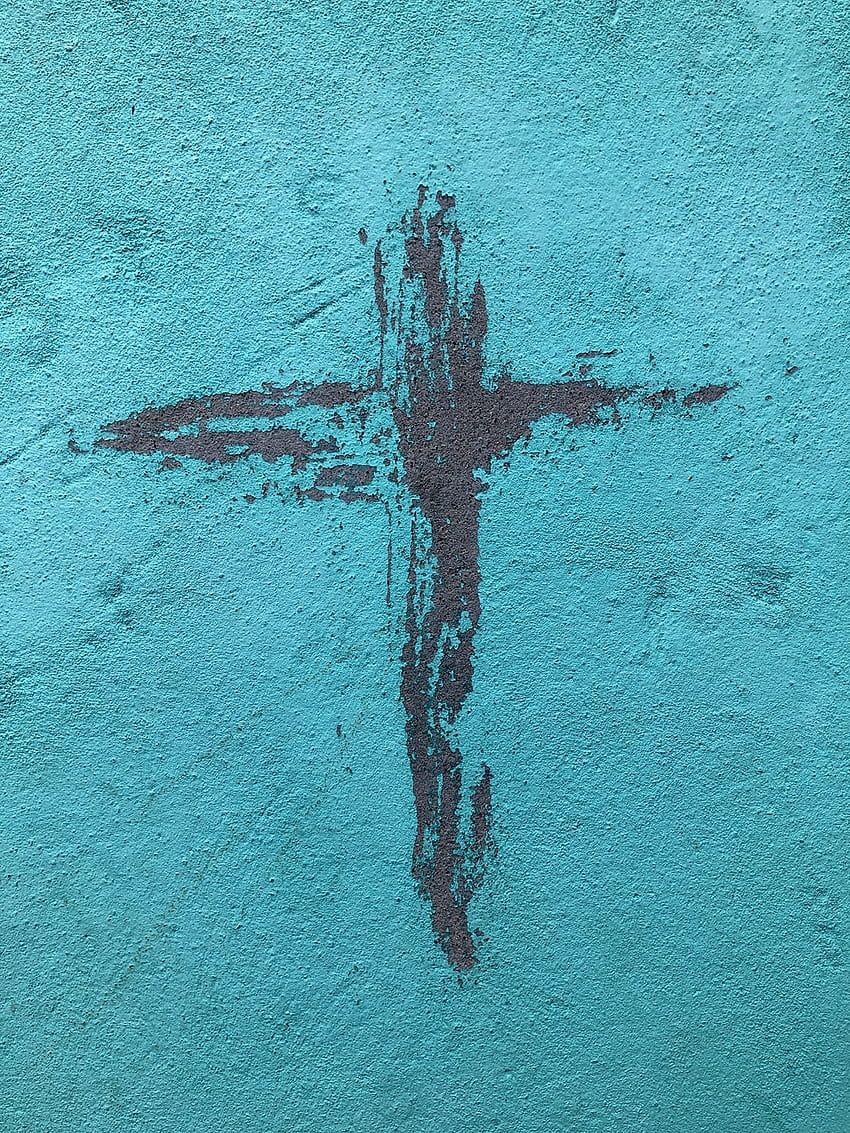 A cross painted on a wall in black against a turquoise background - Jesus
